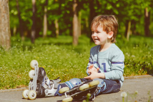 Smiling little boy in rollers sits on walkway at park. Toned image